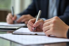 Person writing notes during a client needs assessment meeting